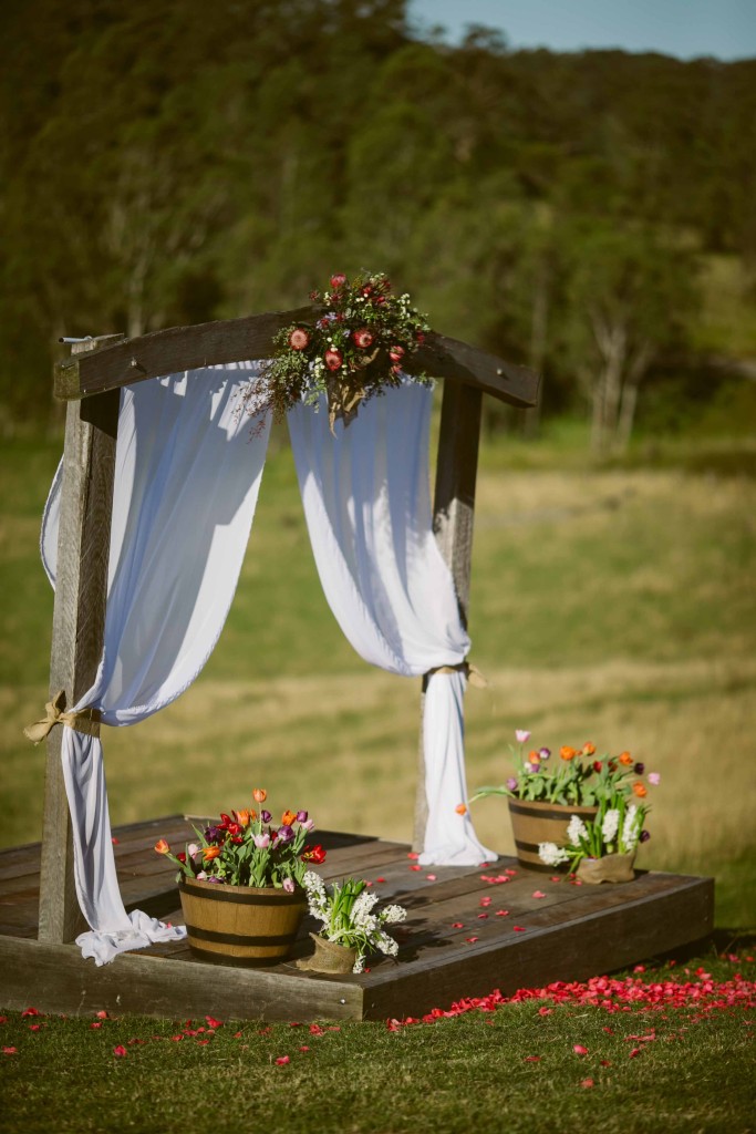 The rustic timber archway decorated with bright coloured flowers and beautiful white flowing Chiffon.